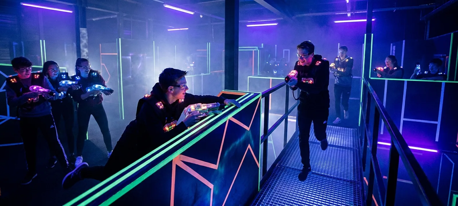 Spieler in einer neonbeleuchteten Lasertag-Arena mit Lichteffekten und Nebel